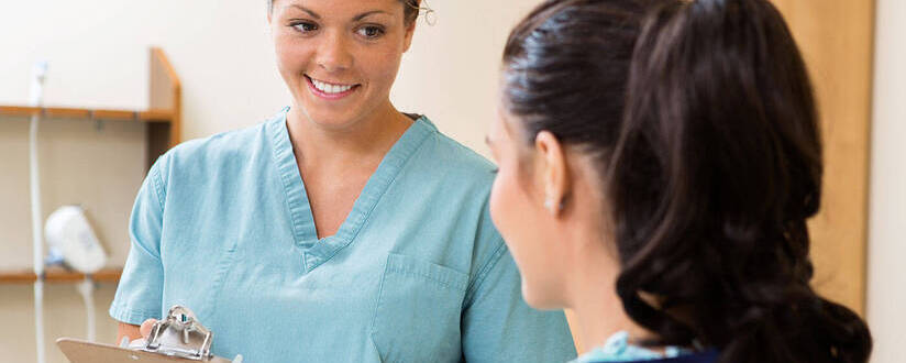 Image of a medical assistant holding a clipboard while talking to a patient