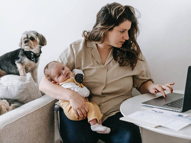 Image of a mother holding her baby while working on a laptop